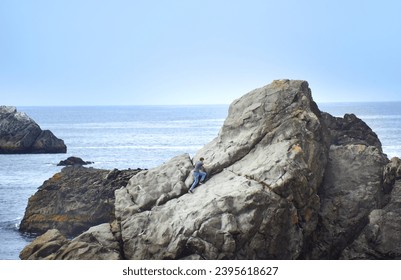 Young man sprints up a large rock formation near Gold Beach, Oregon.  He has on jeans and a grey shirt. - Powered by Shutterstock