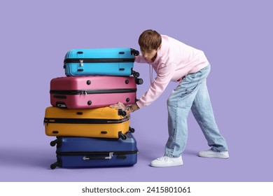 Young man with stack of different suitcases on lilac background