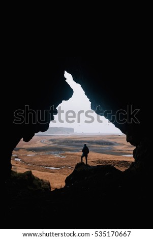 Young man standing alone, back to the camera, at the edge of a cliff, in the cave called Loftsalahellir in the south Iceland. Edges of the cave look like someone's face