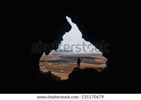 Young man standing alone, back to the camera, at the edge of a cliff, in the cave called Loftsalahellir in the south Iceland. Edges of the cave look like someone's face