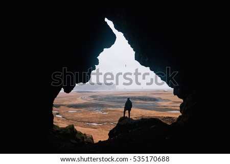 Young man standing alone, back to the camera, at the edge of a cliff, in the cave called Loftsalahellir in the south Iceland. Edges of the cave look like someone's face