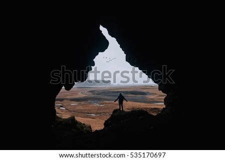 Young man standing alone, back to the camera, at the edge of a cliff, in the cave called Loftsalahellir in the south Iceland. Edges of the cave look like someone's face