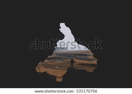 Young man standing alone, back to the camera, at the edge of a cliff, in the cave called Loftsalahellir in the south Iceland. Edges of the cave look like someone's face