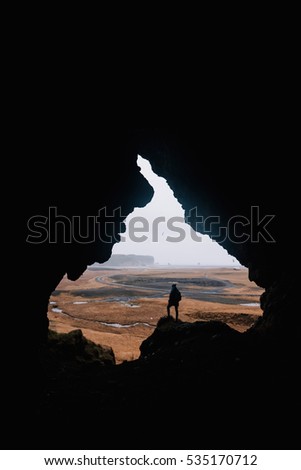 Young man standing alone, back to the camera, at the edge of a cliff, in the cave called Loftsalahellir in the south Iceland. Edges of the cave look like someone's face