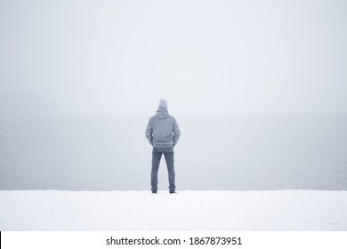 Young man standing alone on snow at lake shore and looking far away. White cold snowy winter day. Thinking about life. Mist over water. Peaceful atmosphere in nature. Back view.  - Powered by Shutterstock