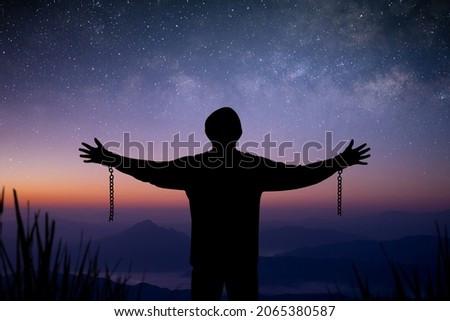 The young man standing alone on top of the mountain with beautiful night sky, star and Milky Way and open both arms with chains on his arms. He felt free from the shackles tied to his arms.