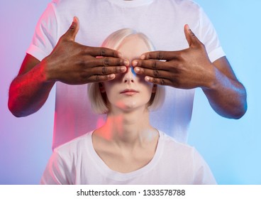 young man is standing behind awesome woman and covering his woman's eyes with hands, isolated blue background, studio shot - Powered by Shutterstock