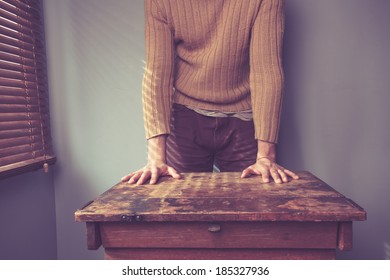 Young Man Is Standing Behind A Desk By The Window