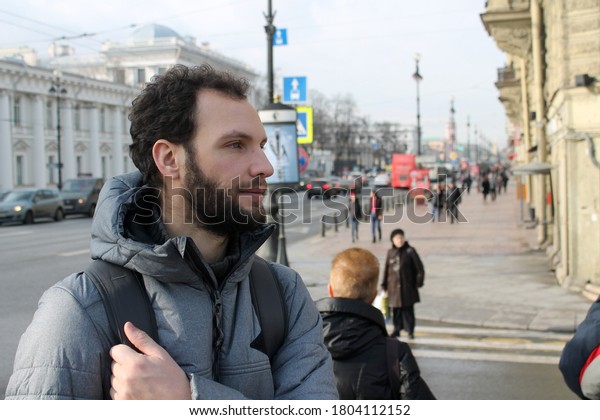 Young man standing at the\
crossroad in Saint Petersburg\'s Nevsky street smiling and looking\
away 