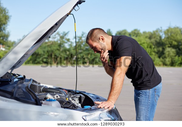 Young man standing\
in front of a broken car