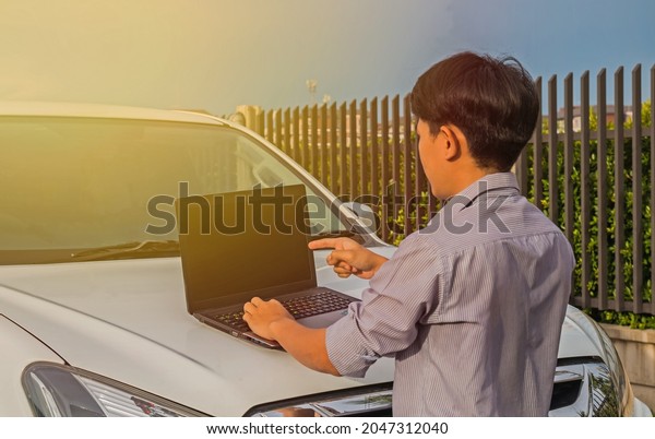a young man standing in front of car and using a
notebook to work