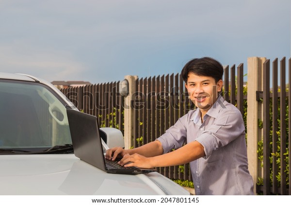 a young man standing in front of car and using a\
notebook to work