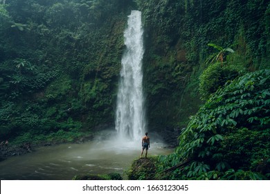 Young man standing in front of powerful Nungnung waterfall. Fun at the waterfalls in Bali. Concept about wanderlust traveling and wilderness culture
 - Powered by Shutterstock