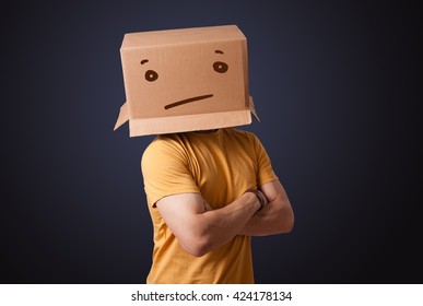 Young Man Standing And Gesturing With A Cardboard Box On His Head With Straight Face