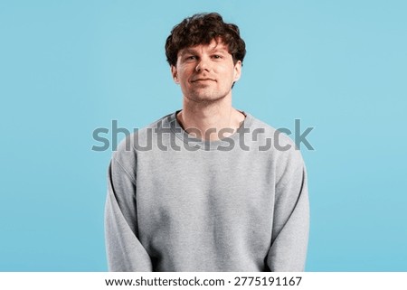 Young man standing and looking at camera with a casual grey sweatshirt, symbolizing confidence, youth, and simplicity