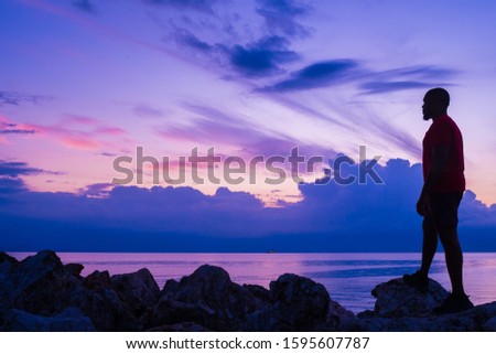 Young man standing on cliff edge staring at endless ocean water, contemplating life and its troubles as he journeys into the unknown. Priorities, decisions and freedom of choice. Stepping out in faith