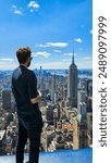 A young man standing on the Summit observatory on One Vanderbuilt enjoying the view towards empire state building in Manhattan, New York City.