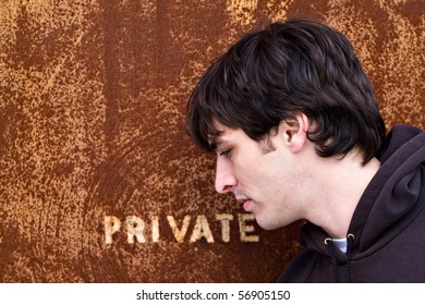 A young man standing outside an old door or entrance that reads PRIVATE.  A great image for any identity theft concept.