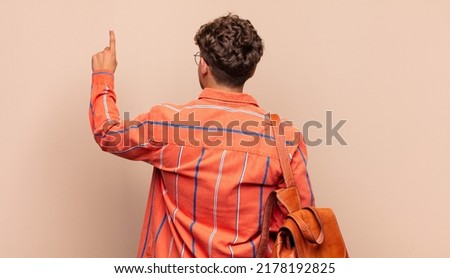 young man standing and pointing to object on copy space, rear view. student concept