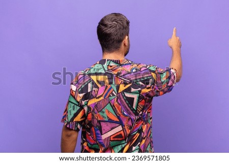 young man standing and pointing to object on copy space, rear view