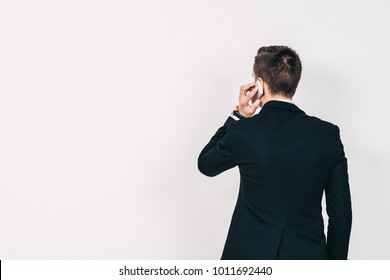 Young Man Standing And Talking On The Phone Over A White Background, Back View, Copy Space