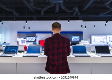 A Young Man Stands Behind His Laptop At The Electronics Store. A Young Man Chooses A Laptop In The Store