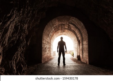 Young man stands in dark concrete tunnel and looks out in the glowing end