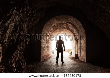 Young man stands in dark concrete tunnel and looks out in the glowing end