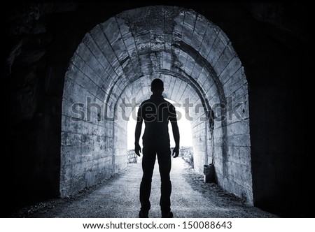 Young man stands in dark tunnel and looks in the glowing end