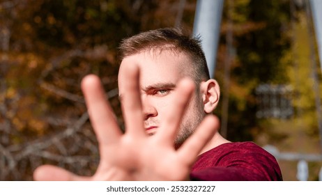 A young man stands outdoors, extending his hand towards the viewer against a backdrop of colorful autumn leaves and a sunny sky. - Powered by Shutterstock