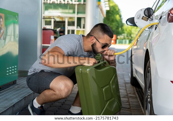 A young man steals gasoline from the gas tank in\
the white car. A young man pumps gasoline from a gas tank into a\
canister. Fuel and oil crisis. The concept of gasoline prices and\
the oil crisis.