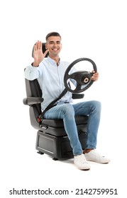 Young Man With Steering Wheel Waving Hand In Car Seat On White Background