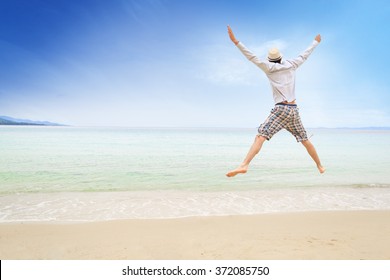 Young Man With A Straw Hat Jumping On The Beach With Arms Wide Open