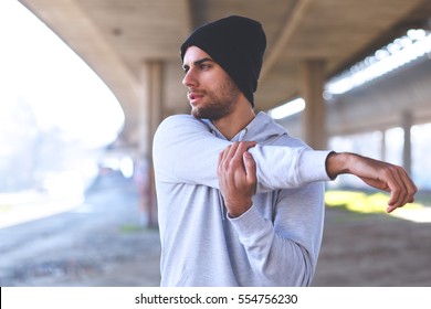 Young Man Stretching His Arm Muscles Under The Bridge Before Running.