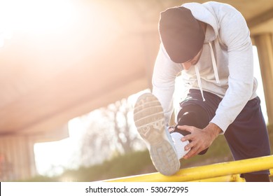 Young Man Stretching His Muscles Under The Bridge Before Running.