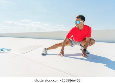 Young man stretching on a rooftop during bright daylight with sunglasses and athletic wear for fitness - Powered by Shutterstock