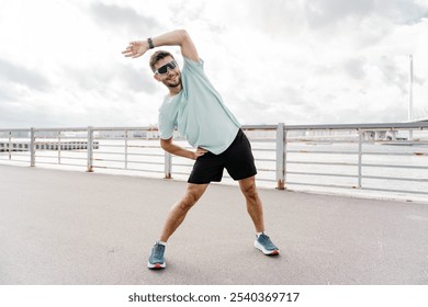 Young Man Stretching on a Waterfront Promenade During a Cloudy Day, Preparing for a Workout or Jog - Powered by Shutterstock