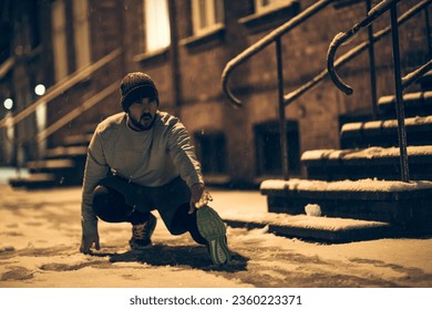 Young man stretching while out jogging and exercising at night during winter and snow in the city - Powered by Shutterstock