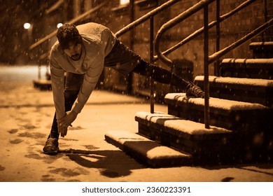 Young man stretching while out jogging and exercising at night during winter and snow in the city - Powered by Shutterstock