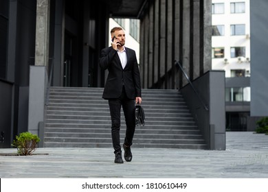 A young man in strict clothes with a bag in his hands goes down the stairs in an urban environment, holds a phone