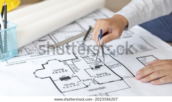 Young man  structural design or engineer is
using a measuring circle around a floor plan or blueprint,
Architect or engineer is designing a building using compasses to
draw the physical
structure.