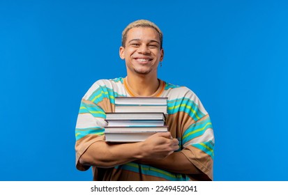 Young man student holds stack of university books from college library on blue background. Happy guy smiles, he is happy to graduate, education abroad concept. High quality photo