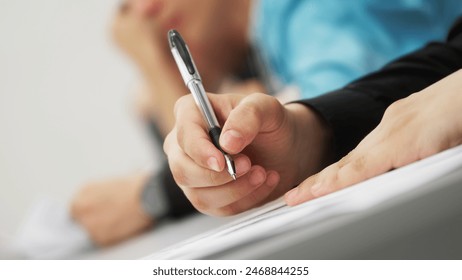 A young man, a student or schoolchild, writes a dictation, an essay or solves an educational problem, sitting at a desk next to other students. Photo. Selective focus. No face. Close-up - Powered by Shutterstock