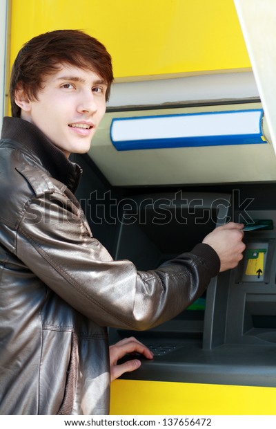 young man student withdrawing money from a  bank\
cash point, outdoors