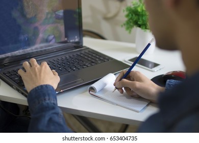 young man studying and working with the computer taking notes