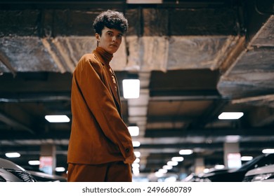 Young man in stylish orange outfit standing confidently in a dimly lit underground parking garage - Powered by Shutterstock