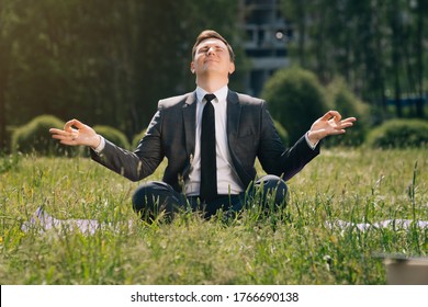 The Young Man Is Stylishly Sitting On The Grass, Working Remotely. Small Business Concept, Freelancer Man Doing Namaste, Cheap Peace Of Mind During Lunch