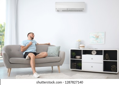 Young Man Suffering From Heat Near Broken Air Conditioner At Home