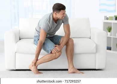 Young Man Suffering From Leg Pain At Home