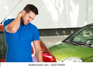 Young Man Suffering From Neck Pain Standing In Front Of Parked Cars